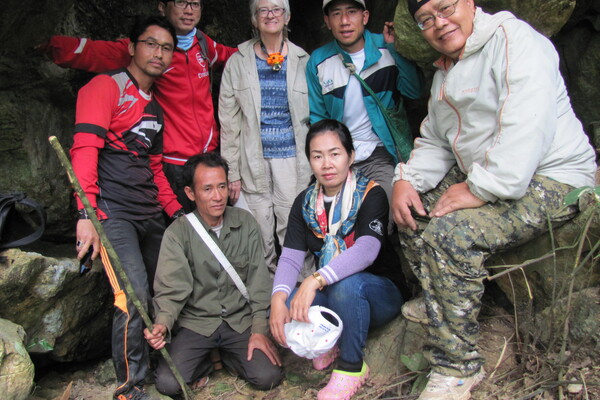 A group of archaeologists and excavators standing and sitting at the entrance of a cave.
