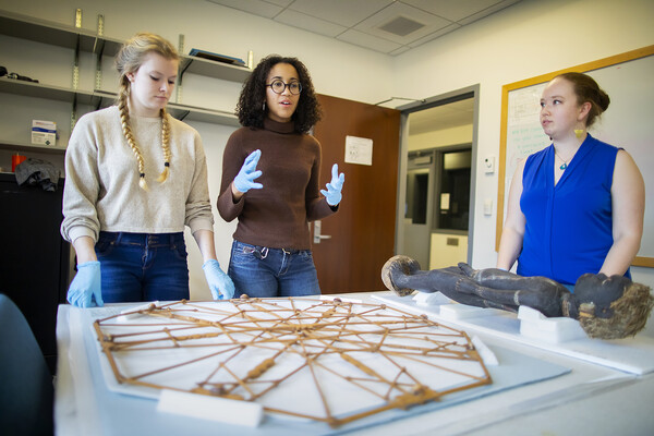 Three woman stand behind museum objects