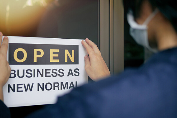 Masked person puts a sign on door that says "OPEN BUSINESS AS NEW NORMAL"