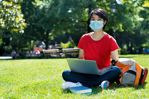 Student in mask sitting on grass