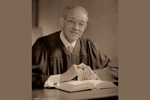 Historical photo of Raymond Pace Alexander wearing a judge robes seated at a table over an open book.