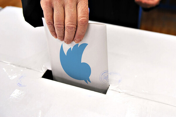 Hand stuffing a paper in a ballot box with the blue Twitter logo visible on the paper.