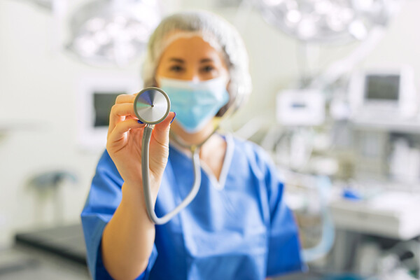 Medical professional in mask and PPE holding up a stethoscope in a hospital room.