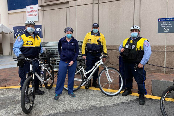 Penn DPS police officers wearing face-coverings standing with bikes in front building on campus