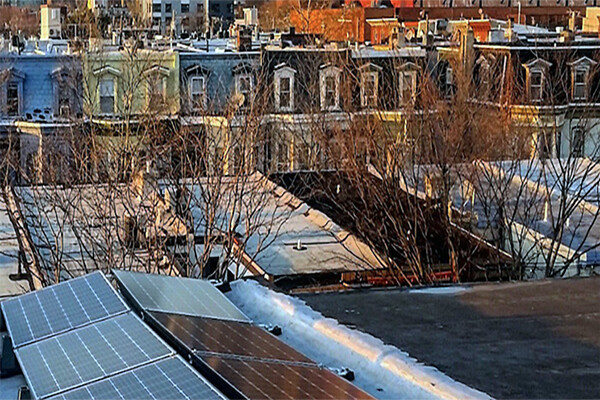 Philadelphia rowhouse roofs with solar panels in foreground and city skyline in background.