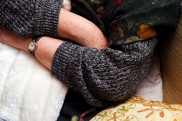 Middle-aged person sick in bed with water bottle in sweater and scarf.