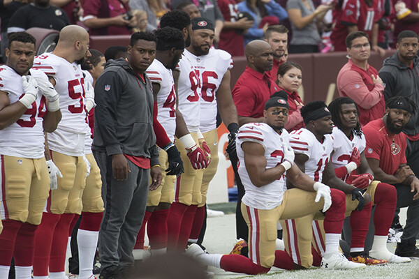 Members of the 49ers football team kneeling on the field before a game.