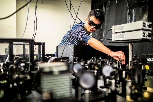 a person wearing darkened glasses adjusting lenses on an optics table