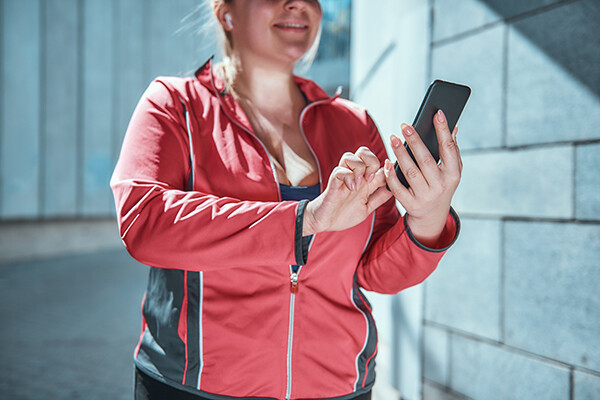 person in exercise gear looking at their phone with earbuds in.