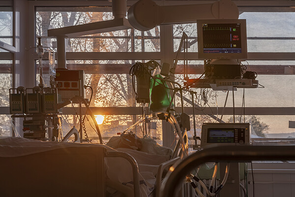 Morning sun shining through a window in a hospital room with a patient lying in bed attached to tubes and monitors.