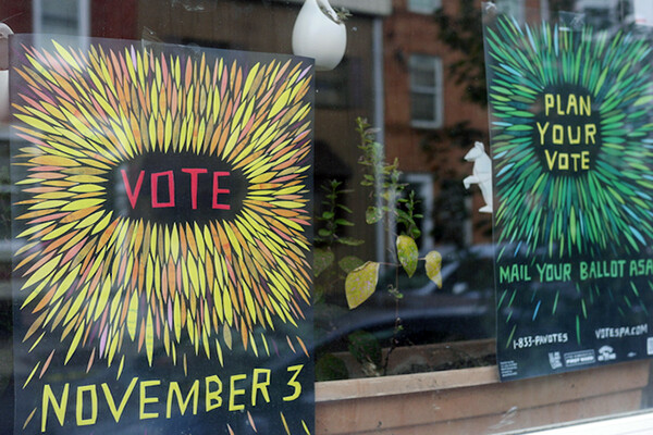 Two handmade signs in a window that read VOTE NOVEMBER 3 and PLAN YOUR VOTE.