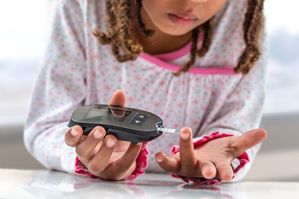 A young child testing their blood sugar level with a finger prick machine.