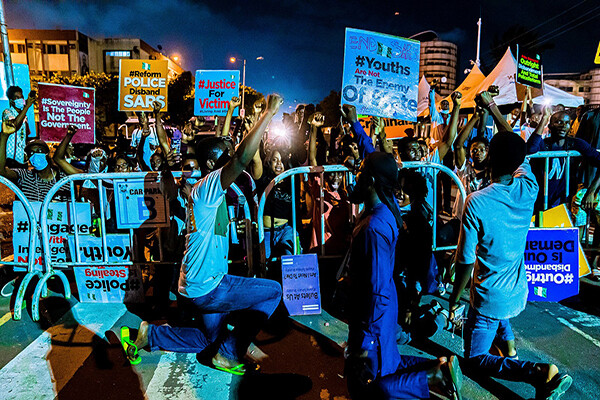 A group of protesters kneels holding signs aloft on a city street at night