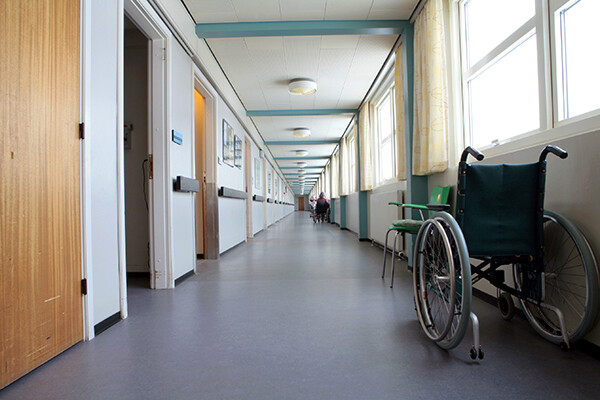 Nursing home hallway with an empty wheelchair parked outside an open door.