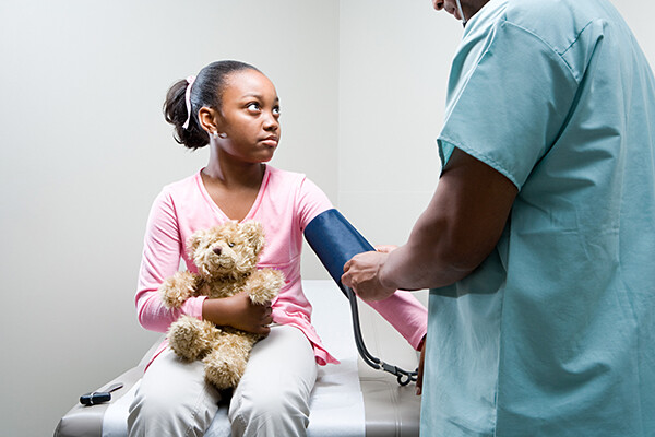 Adolescent child holding a teddy bear having their blood pressure taken by a nurse.