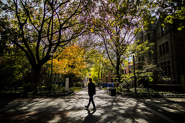 Person walking along Locust Walk at a walkway intersection with colorful autumn leaves.