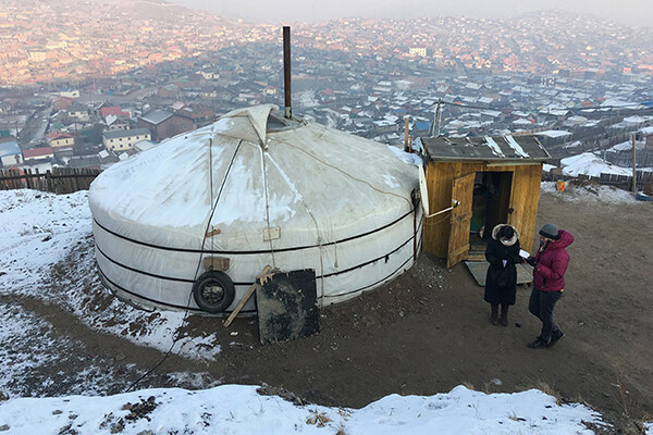 Two people standing beside a Mongolian ger on a hill with Ulaanbaatar in the background.