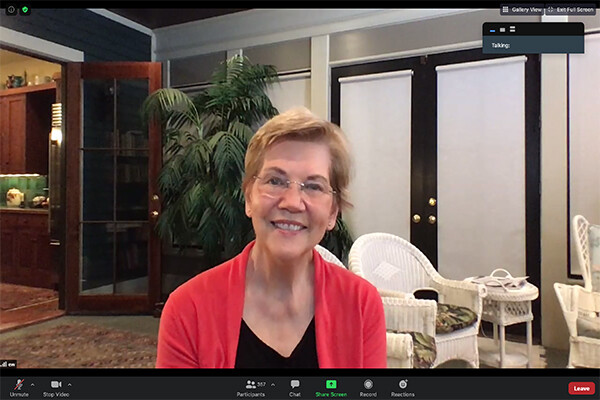 Woman with short blond hair, glasses, red cardigan and black t-shirt smiles during a Zoom call