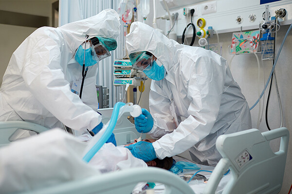 Two medical professionals in full PPE intubate a patient on a hospital bed.