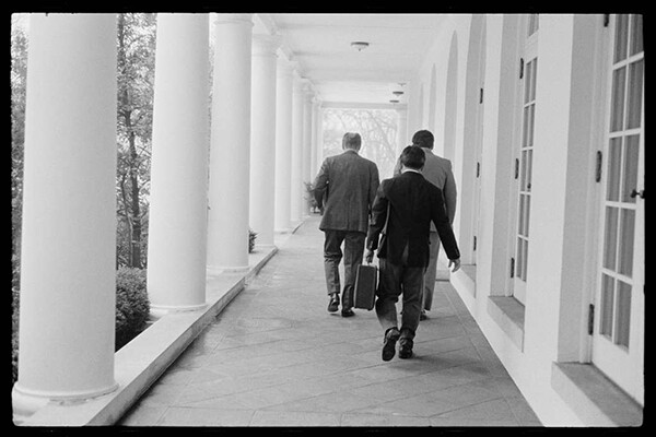 President Gerald Ford and two others are see from behind walking down a White House outdoor walkway in 1975