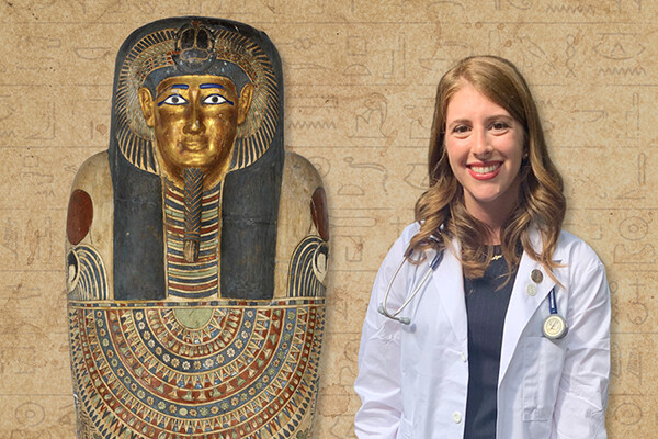 Charlotte Tisch wearing a white medical coat and stethoscope standing next to a fresco of a mummy.