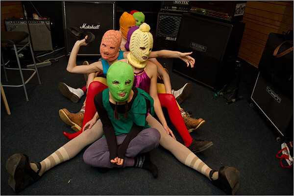 Group of women wearing colorful knitted balaclavas sit on the floor in front of Marshall speakers and amps