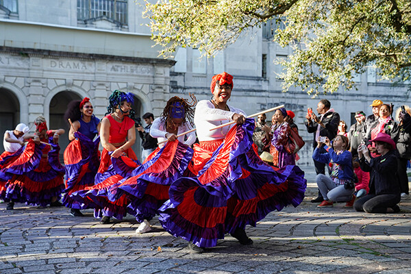 Street dancers in colorful costumes being cheered on by bystanders 