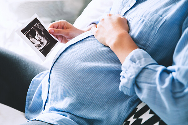 Pregnant person sitting on couch holding an ultrasound photo.