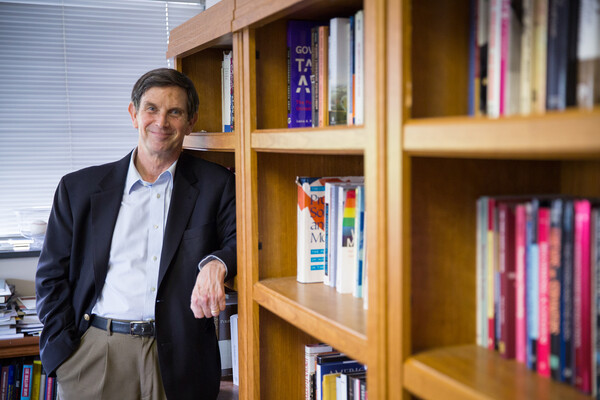 Rogers Smith stands, smiling, by bookshelves in his office.