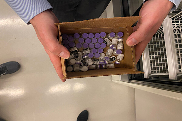 Hands holding a box of COVID vaccine vials.