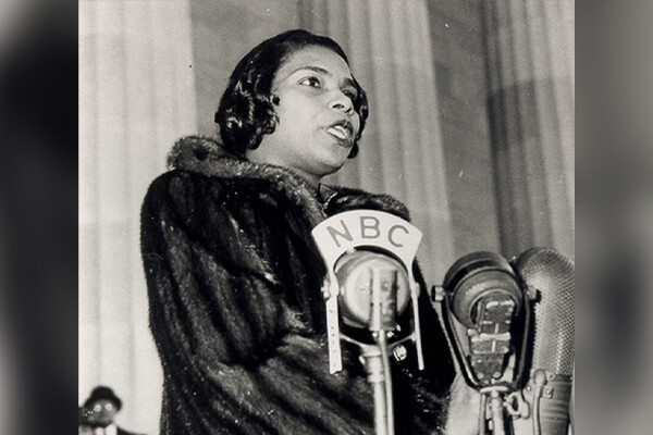 Woman in a fur coat sings before several microphones; one says 'NBC'