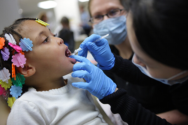 Young child has their teeth examined by a dental expert with an assistant looking on.