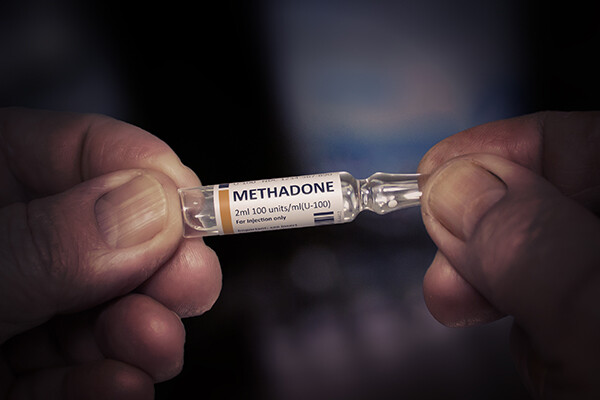 Fingers holding a small glass vial of methadone.