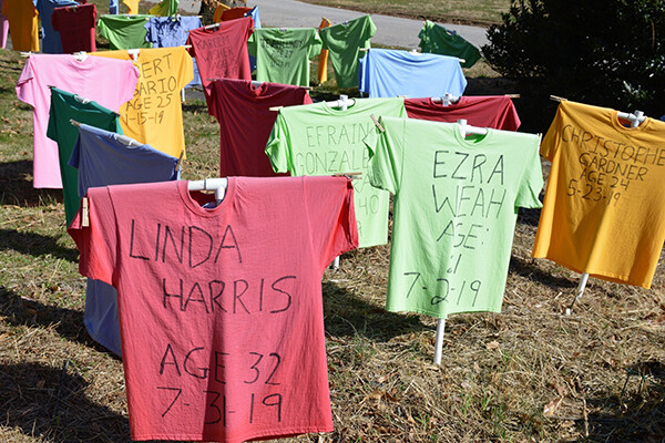 Yard full of standing colorful t-shirts with the names of people killed by guns in black marker written across them.