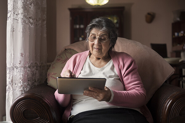 Senior citizen sitting in a chair by the window using an iPad.