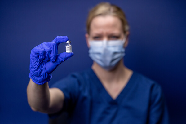 nurse holding the covid vaccine against blue background