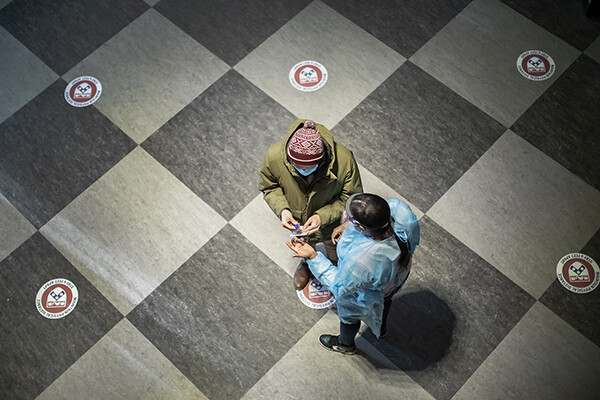 Overhead view of a medical worker in full PPE discussing a COVID spit test with a student on campus.