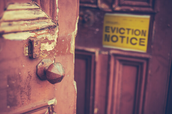 A close-up of an old chipping door. Blurred in the background is a sign that reads "EVICTION NOTICE" in all capital letters.