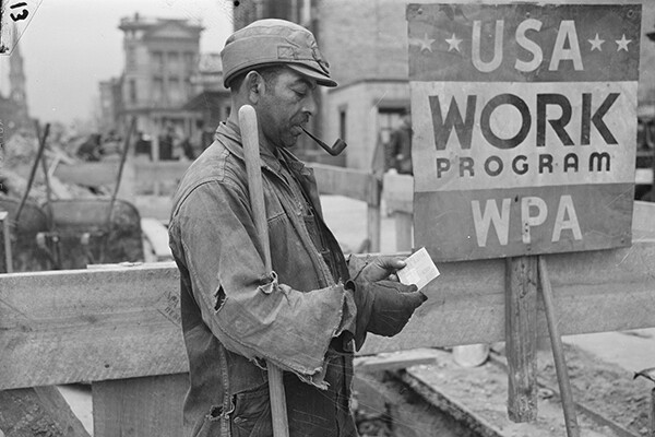 Man in laborer clothes holds shovel, smokes a pipe and looks at his paycheck by a sign reading "USA Work Program WPA"