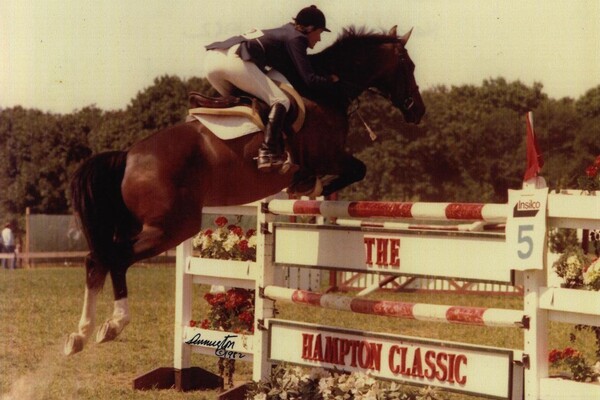 Older photo of equestrian on horse jumping over barrier that reads The Hampton Classic