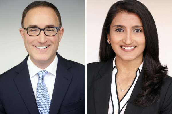 Headshots of two people. On the left is a person with glasses wearing a blazer, white shirt and blue tie. On the right is a person in a black blazer, black-and-white blouse and visible necklace. Both are smiling.