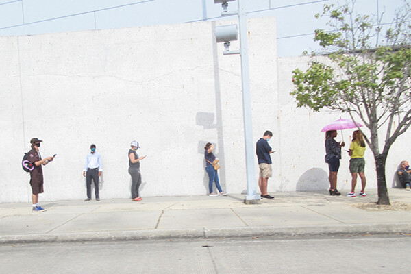 Voters stand in line outside against a white wall, socially distanced and wearing masks.
