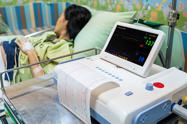 Pregnant person in a hospital bed with an EKG monitor beside the bed.