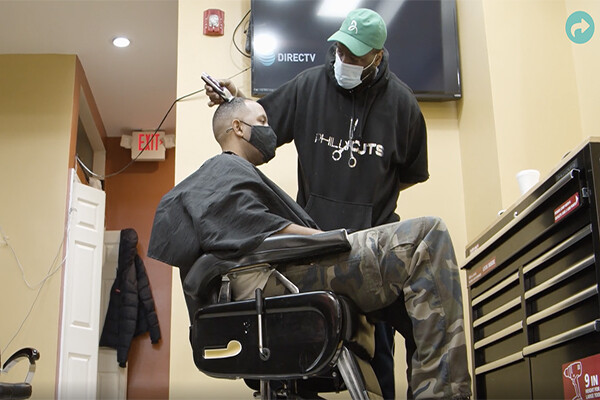 A person wearing a face mask gets their hair buzzed by a barber also wearing a face mask in a West Philly barbershop.
