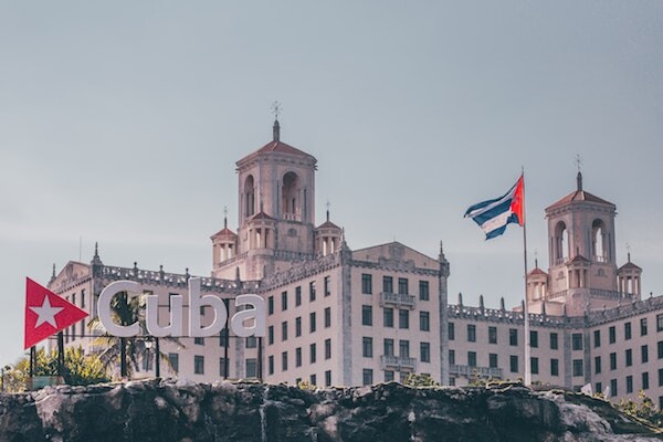 A larger building flies the Cuban flag. A sign in front says "Cuba"