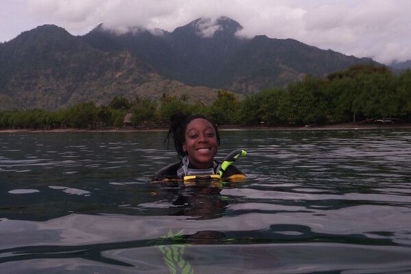 Camille Gaynus in scuba gear in the water with mountains in the background