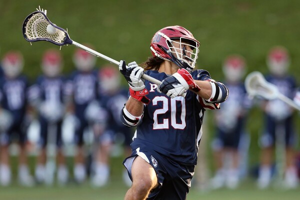 Adam Goldner, wearing his blue Penn jersey, makes a move with his stick with the ball in the net.