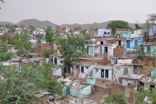Rows of houses with corrugated metal roofs are interspersed with trees. A mountain range is in the background 