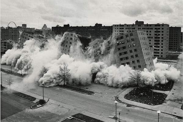A black and white image of high-rise buildings collapsing in a cloud of dust