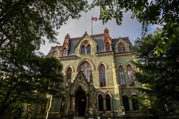 a photograph of Penn's college hall framed by green leaves during the summer